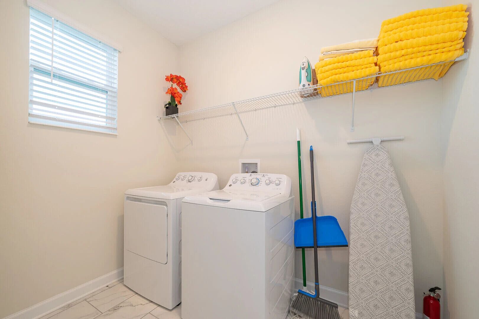 A laundry room with two washing machines, a drying rack with yellow towels, a broom, and a fire extinguisher.