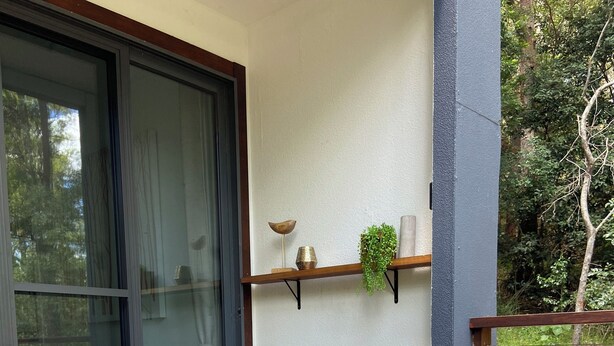 Deux fauteuils de jardin avec des coussins à motifs floraux, placés sur une terrasse en bois, une porte vitrée et une étagère ornée d’objets décoratifs.