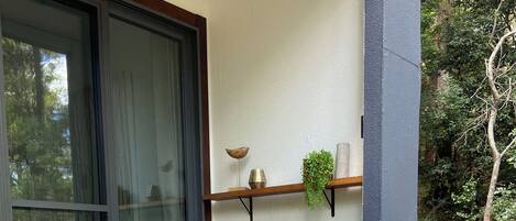 Two lounge chairs with floral cushions on a wooden deck, a glass door, and a shelf with decorative items.