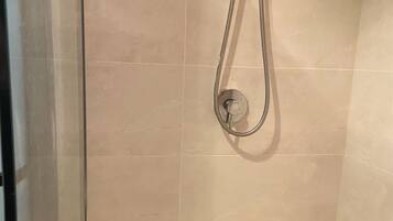 Een douche met een handdouche en een wandmengkraan. Er is een zwarte handdoekhouder met twee flessen erop.