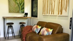 Un salon avec un canapé marron, des coussins colorés, un tapis blanc, une table basse et un téléviseur.