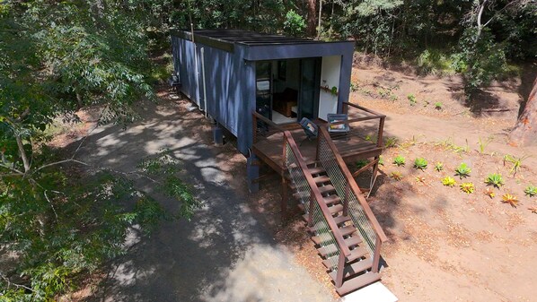 A small, modern cabin with a metal staircase leading up to a wooden deck.