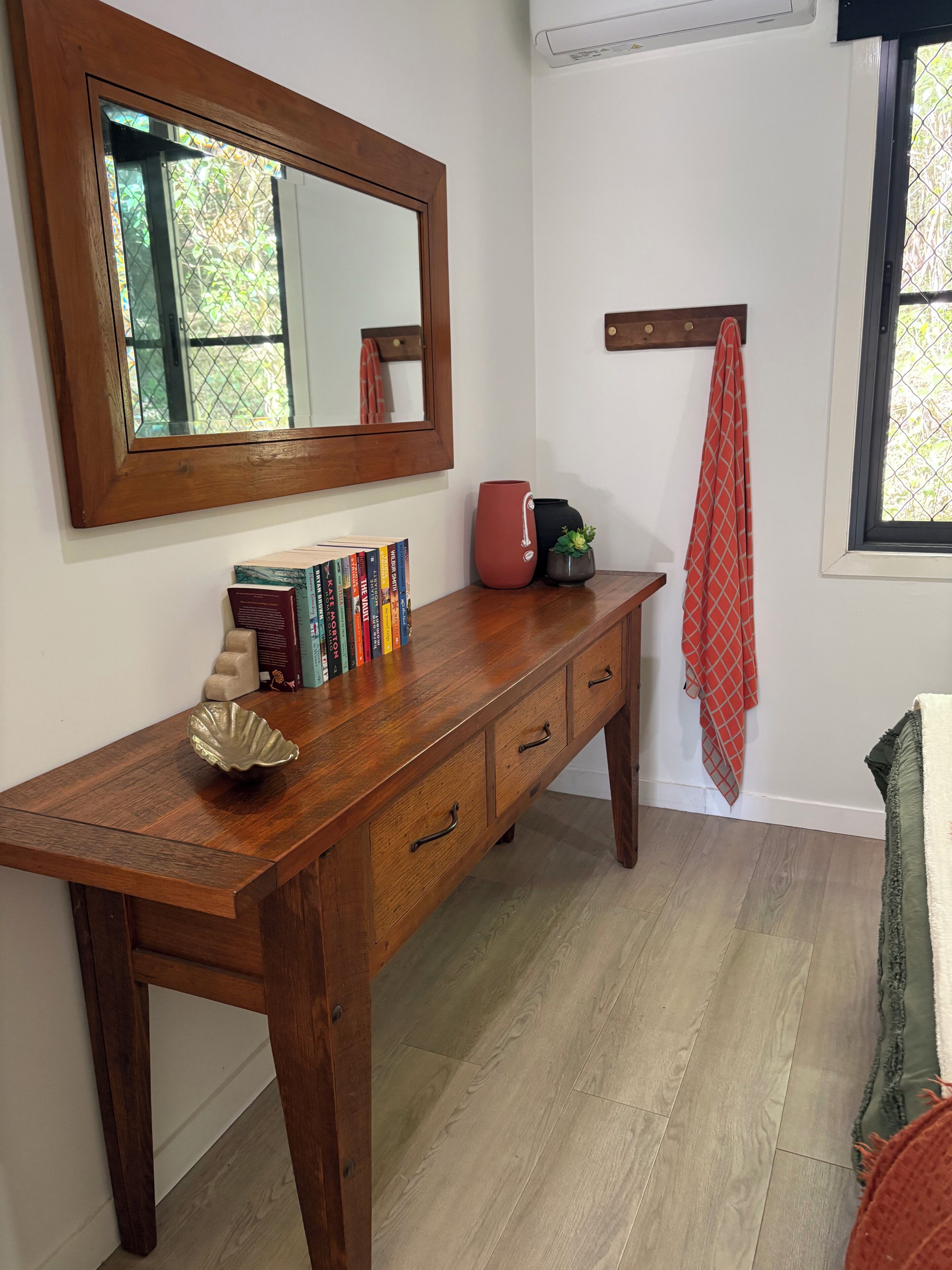 A wooden desk with books, a vase, and a mirror.