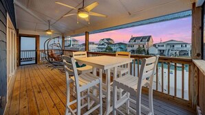 A wooden deck with a table and chairs, a ceiling fan, and a view of houses across the water. - Summer Breeze | 5BR Waterfront Home w Heated Pool (North Myrtle Beach)