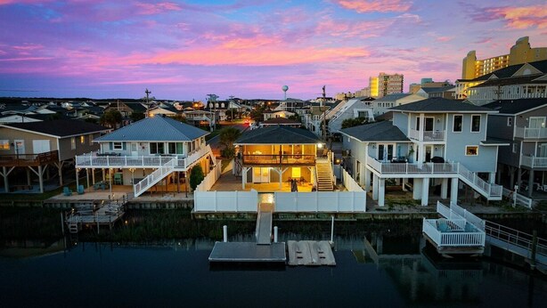 A waterfront property with multiple houses, a dock, and a boat. - Summer Breeze | 5BR Waterfront Home w Heated Pool (North Myrtle Beach)