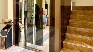 Un vestíbulo de hotel con un ascensor de vidrio, una escalera de mármol y un mostrador de recepción.