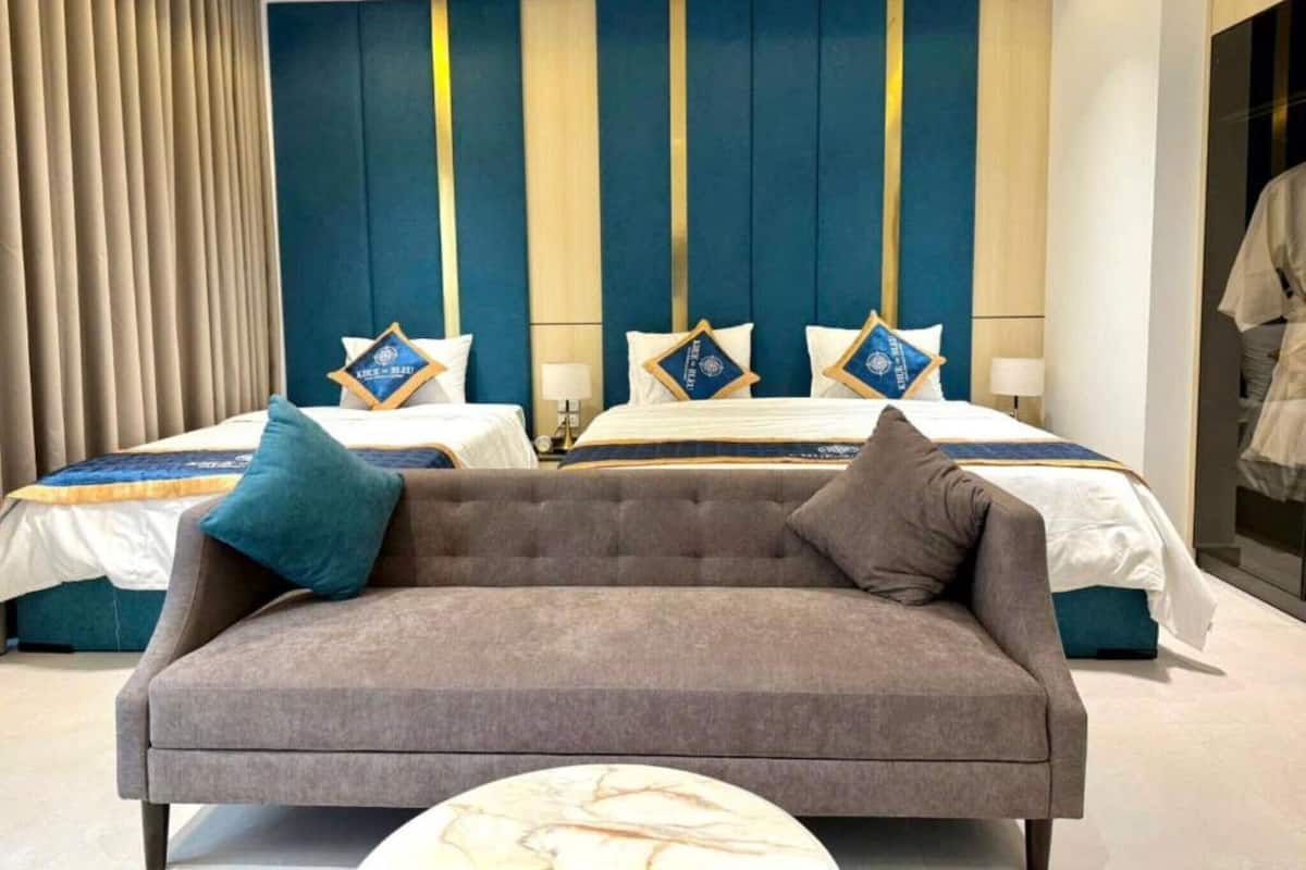 Une chambre d’hôtel avec deux lits, un canapé gris et une table basse en marbre.