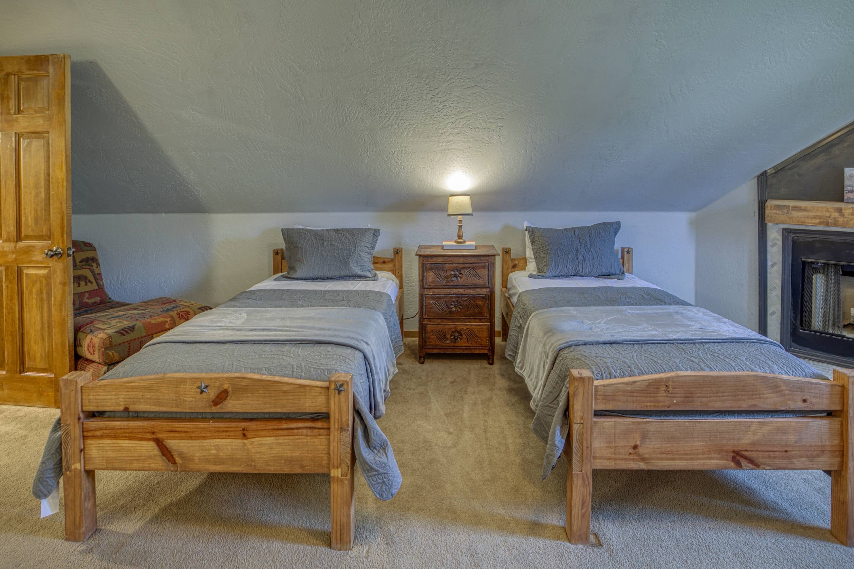 A bedroom with two wooden beds, a nightstand with a lamp, and a fireplace.