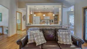 A spacious living room with a leather sofa, a kitchen in the background, and pendant lighting. - Mountain Views, Pet Friendly, New Hot Tub, Fenced Yard, Near Trails! (Pagosa Springs)