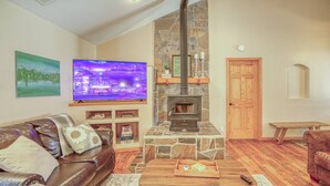 A cozy living room with a stone fireplace, leather sofa, and a flat-screen TV. - Mountain Views, Pet Friendly, New Hot Tub, Fenced Yard, Near Trails! (Pagosa Springs)