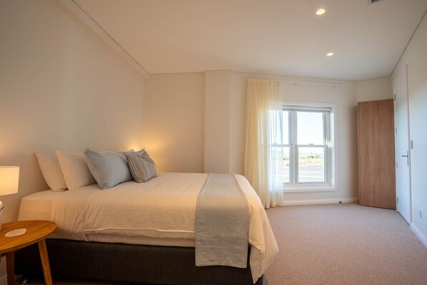 Une chambre à coucher avec un lit, une table de chevet, une fenêtre avec des rideaux et une porte.