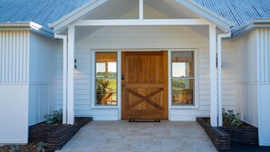 A modern house with a prominent wooden front door, white siding, and a sloped metal roof. - Estate House Villas - Crooked River Estate (Gerringong)