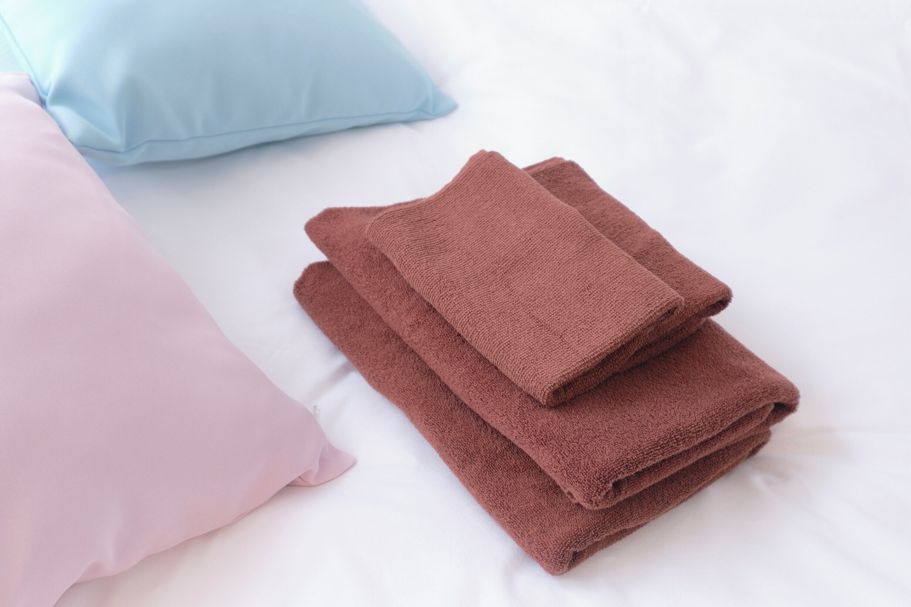 A neatly made bed with pink and brown towels and a light blue pillow.