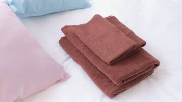 A neatly made bed with pink and brown towels and a light blue pillow.