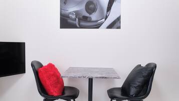 A room with a grey marble table, two black chairs, one with a red cushion, and a wall-mounted TV.