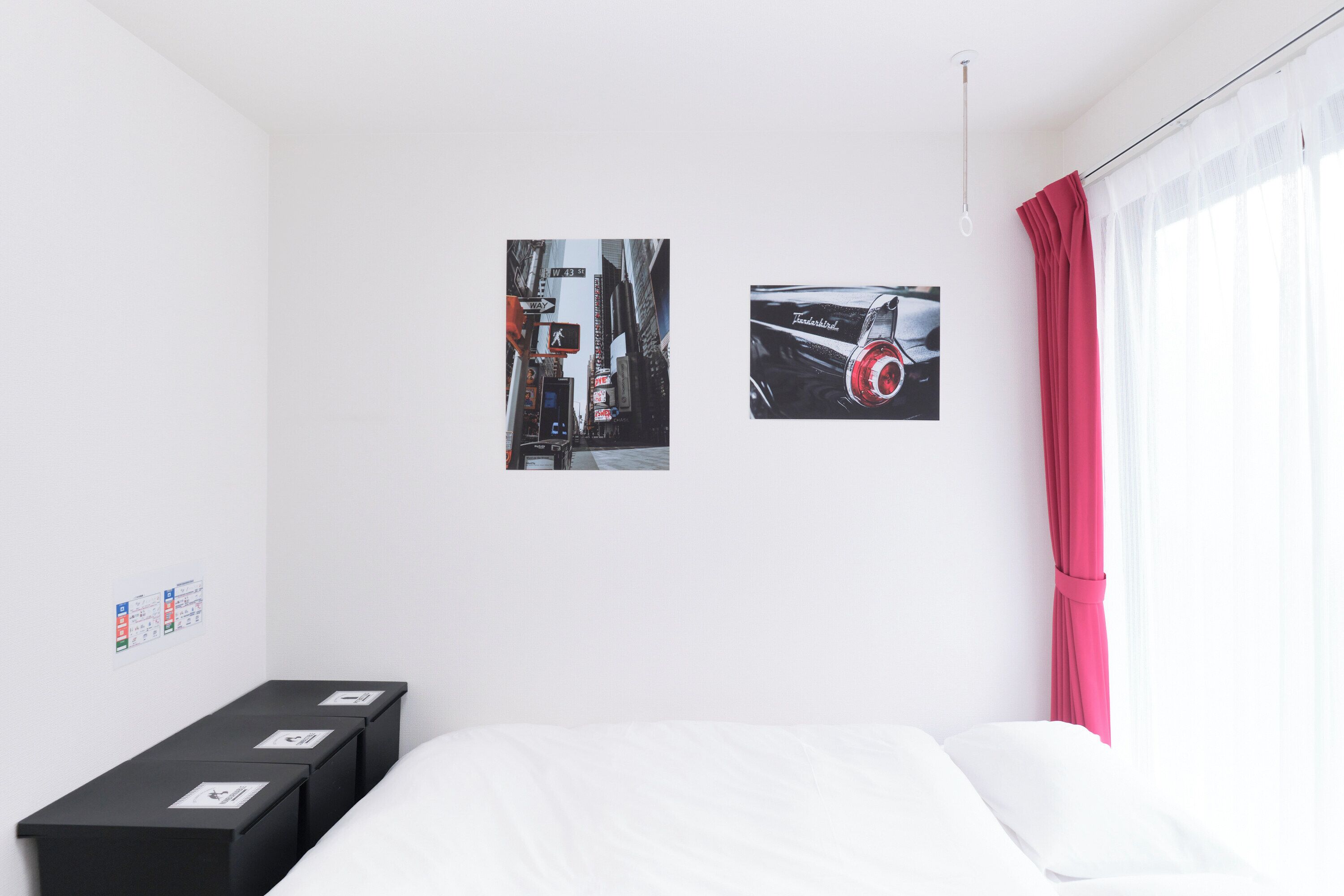 A hotel room with a bed, a black storage unit, and two framed pictures on the wall.