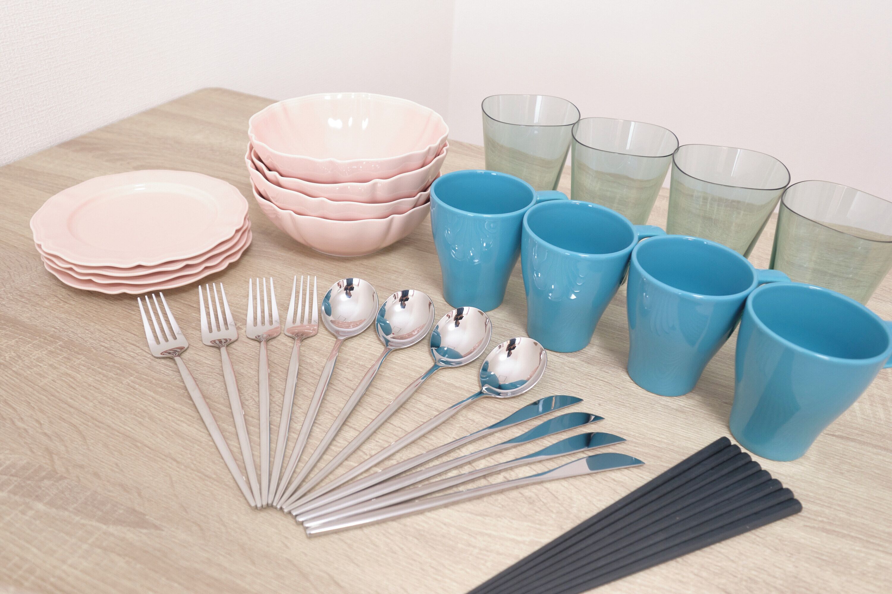 A table with stacks of pink and blue plates, bowls, and cups, along with silverware and black straws.