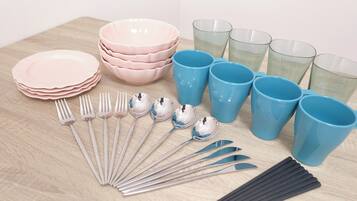 A table with stacks of pink and blue plates, bowls, and cups, along with silverware and black straws.