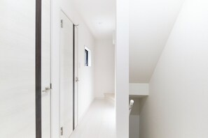 A hallway with white walls and a tiled floor, leading to a door with a small window. - Seacrest Nakanobu by Tranova (Tokyo)