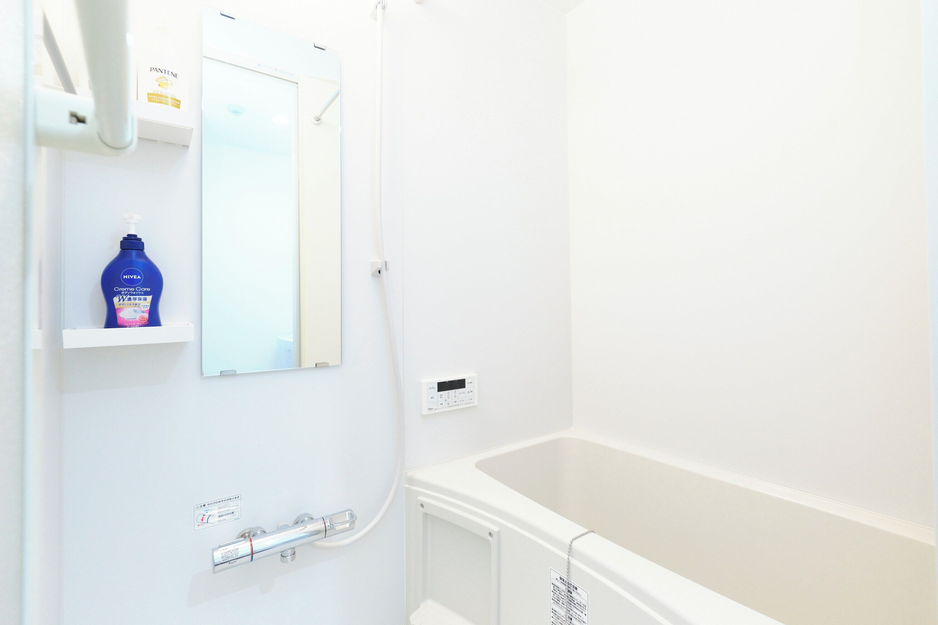 A bathroom with a bathtub, a mirror, a hand soap dispenser, and a shower control panel.