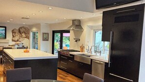 A modern kitchen with a large island, dark cabinetry, and a flat-screen TV mounted above the island. - 4-bedroom house in wonderful Stevenson Ranch with WiFi, AC (Stevenson Ranch)