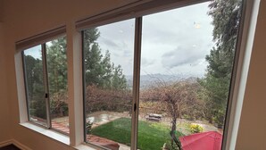 A room with three large windows overlooking a backyard with a lawn, trees, and a red umbrella. - 4-bedroom house in wonderful Stevenson Ranch with WiFi, AC (Stevenson Ranch)