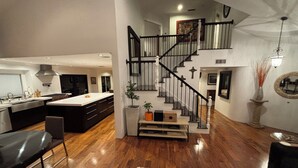 A modern kitchen with a central island, a dining area with a black table and chairs, and a staircase leading to an upper level. - 4-bedroom house in wonderful Stevenson Ranch with WiFi, AC (Stevenson Ranch)