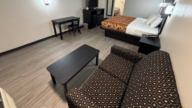 A hotel room with a bed, a sofa, a desk, a chair, and a television.