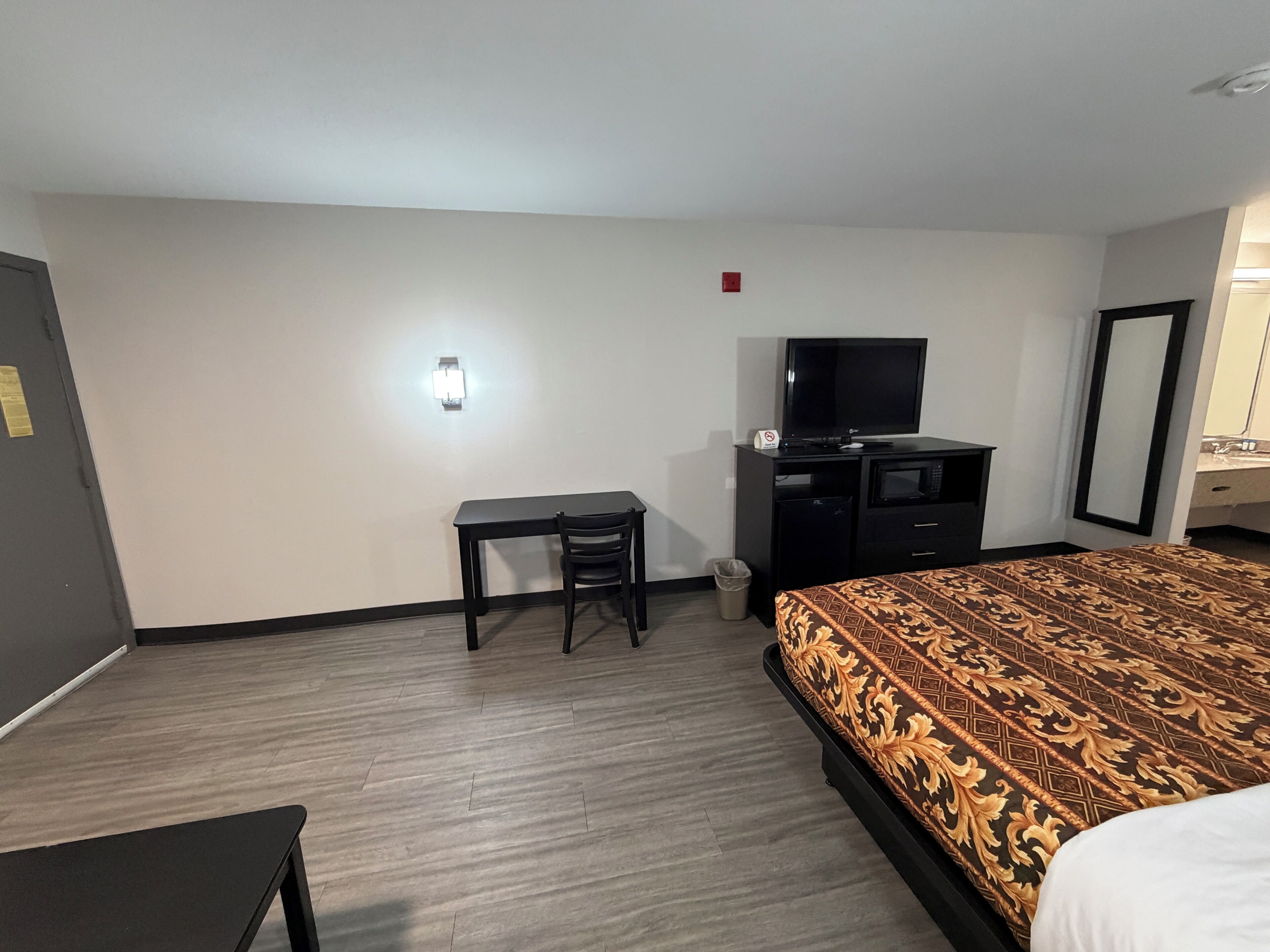 A hotel room with a bed, a desk, a television, a microwave, and a trash bin.