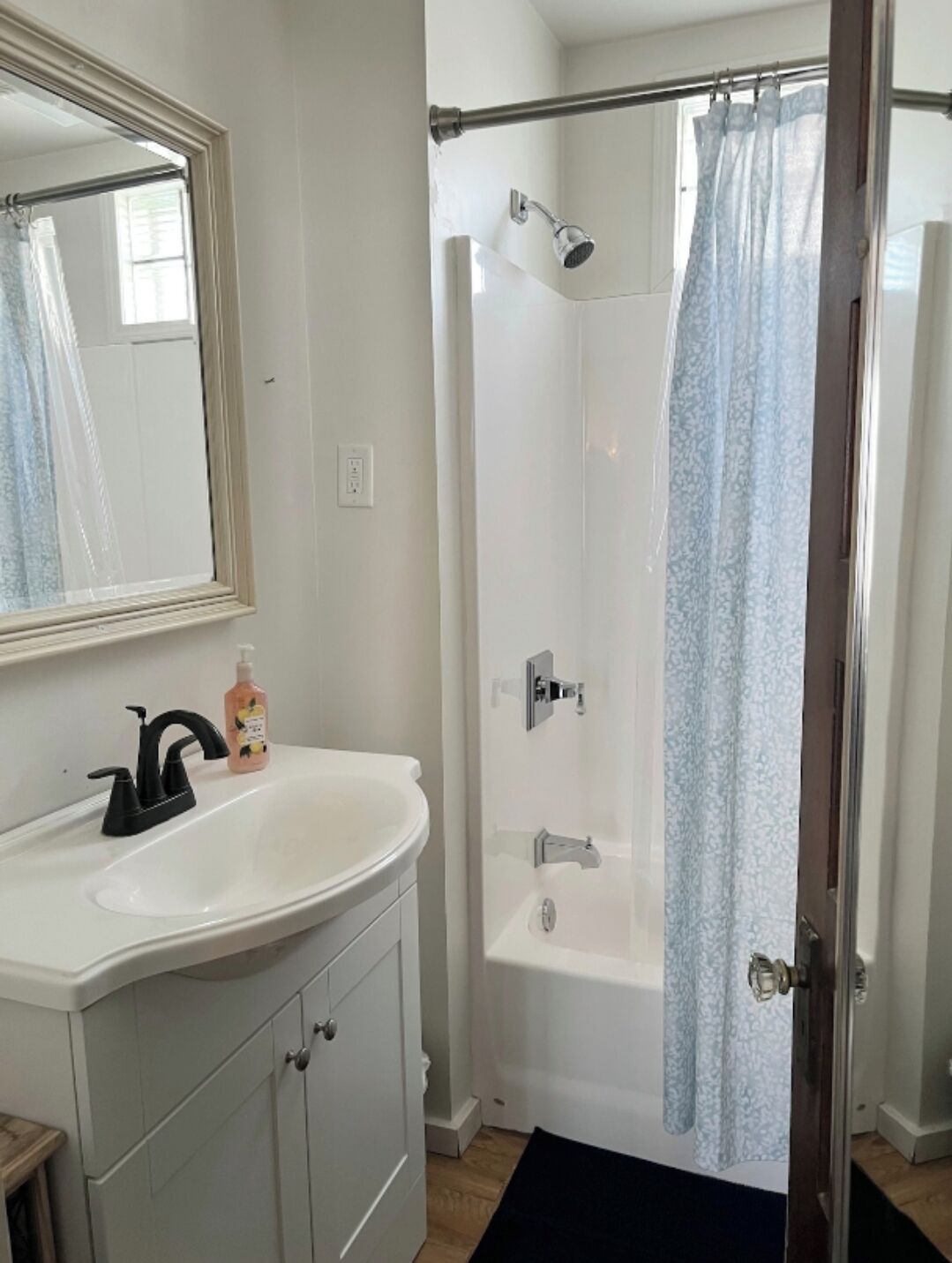 A bathroom with a white sink, a mirror, a shower with a glass door, and a black bath mat.