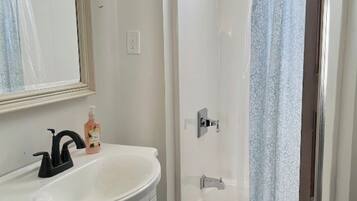 A bathroom with a white sink, a mirror, a shower with a glass door, and a black bath mat.