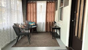 Una habitación acogedora con zona de estar que incluye dos sillas y una mesita, una ventana con cortinas y una puerta con ventanal.