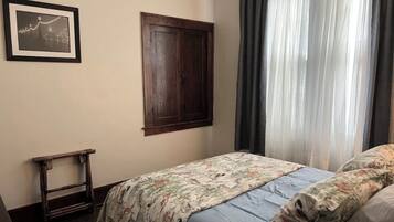 A bedroom with a bed, a wooden wardrobe, a small table, and a framed picture on the wall.