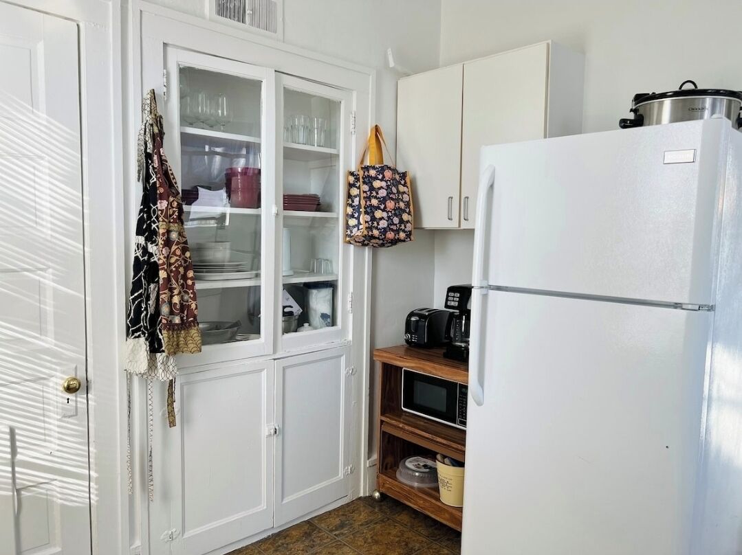 Una cocina compacta con armarios blancos, un refrigerador blanco y un microondas sobre una estantería de madera.