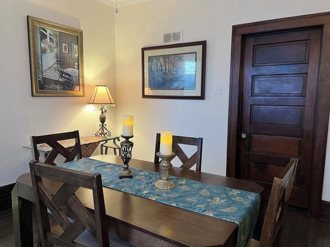 A dining area with a table set for four, two candles, framed pictures on the wall, and a wooden door.