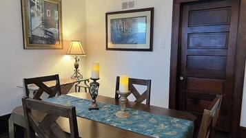 A dining area with a table set for four, two candles, framed pictures on the wall, and a wooden door.