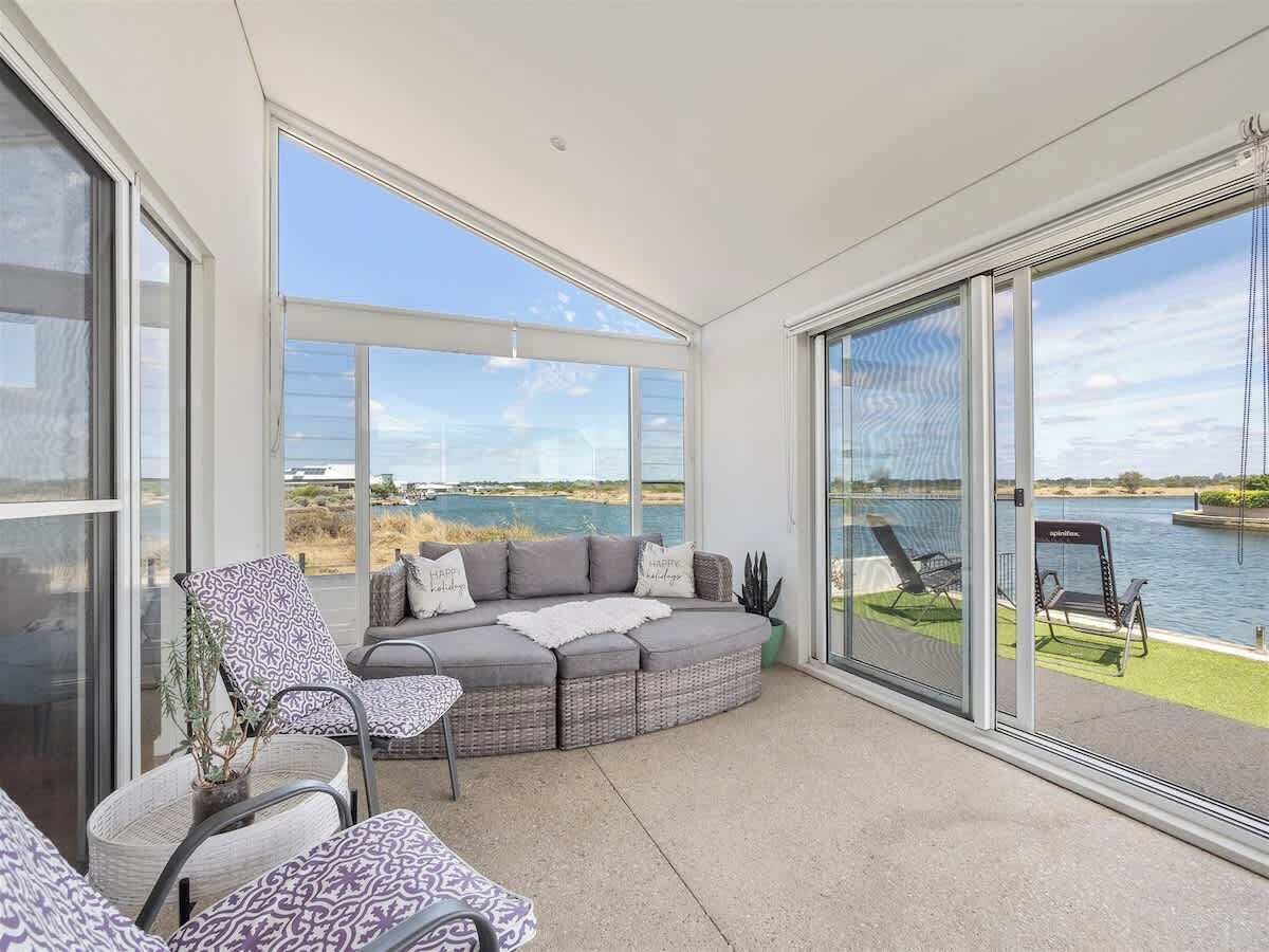 A balcony with a seating area, a view of a body of water, and a clear sky.