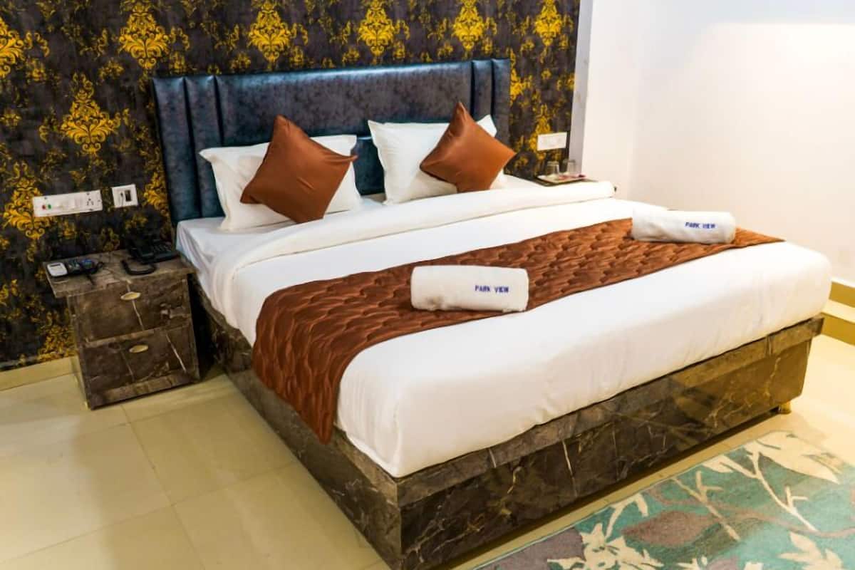 A hotel room with a large bed, a dark headboard, and a patterned wall.