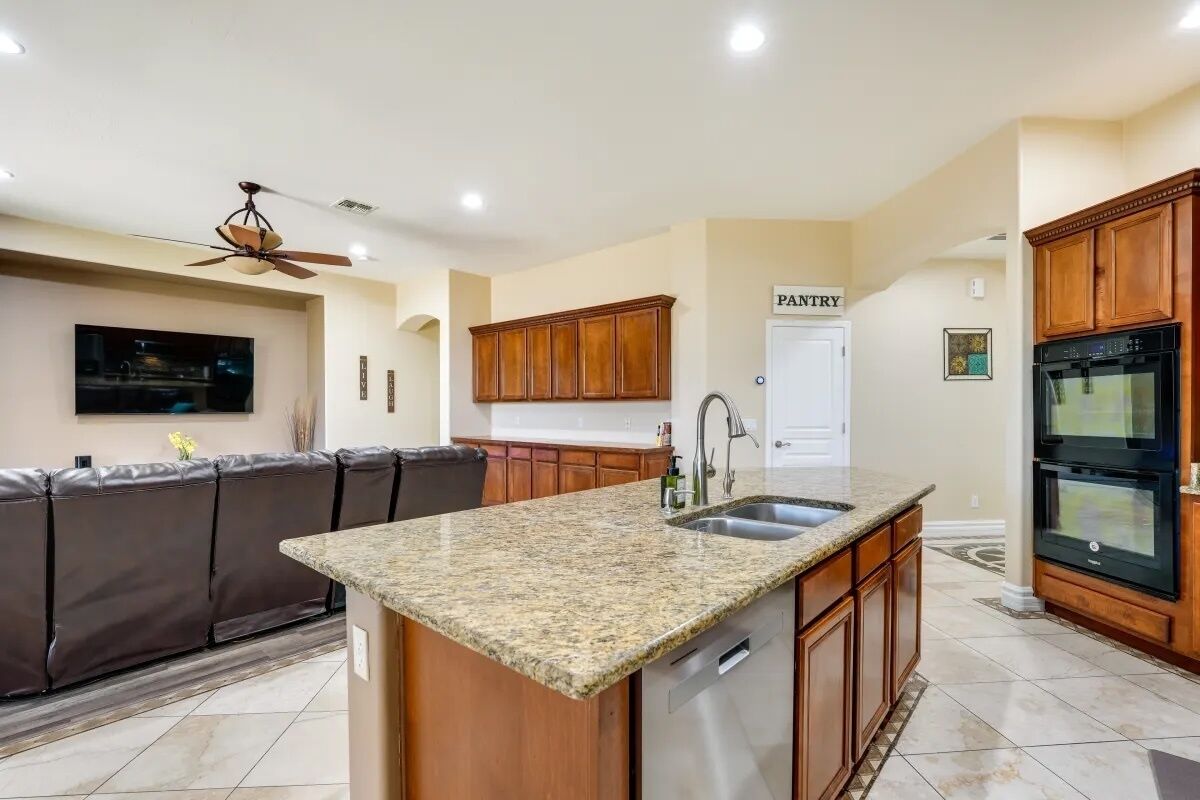 A modern kitchen with granite countertops, wooden cabinets, a built-in oven, and a ceiling fan.