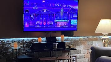 A flat-screen TV mounted on a stone wall, with a small table and a lamp in front.