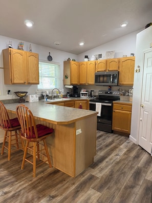 Una cocina moderna con armarios de madera, una isla central con taburetes y un horno empotrado, además de un microondas.
