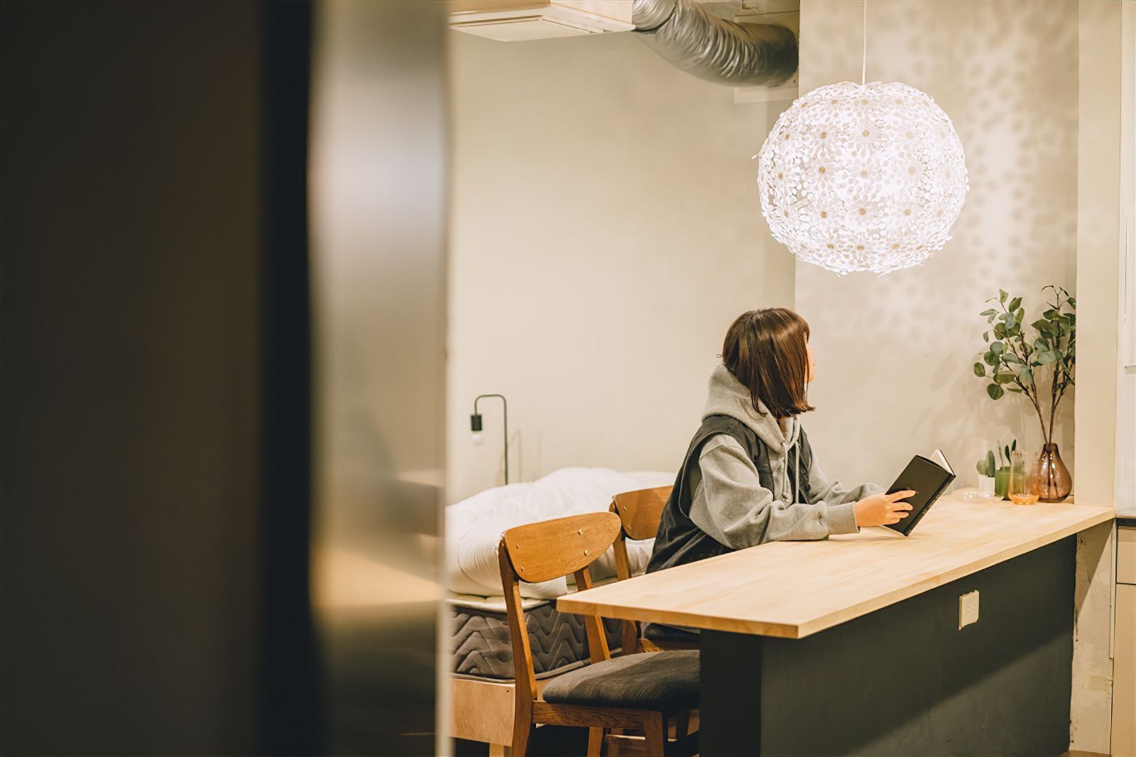 A person reading at a wooden desk in a room with a large, textured pendant light.
