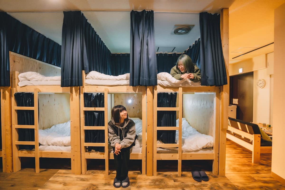 A dormitory room with bunk beds, wooden floors, and a clock on the wall.