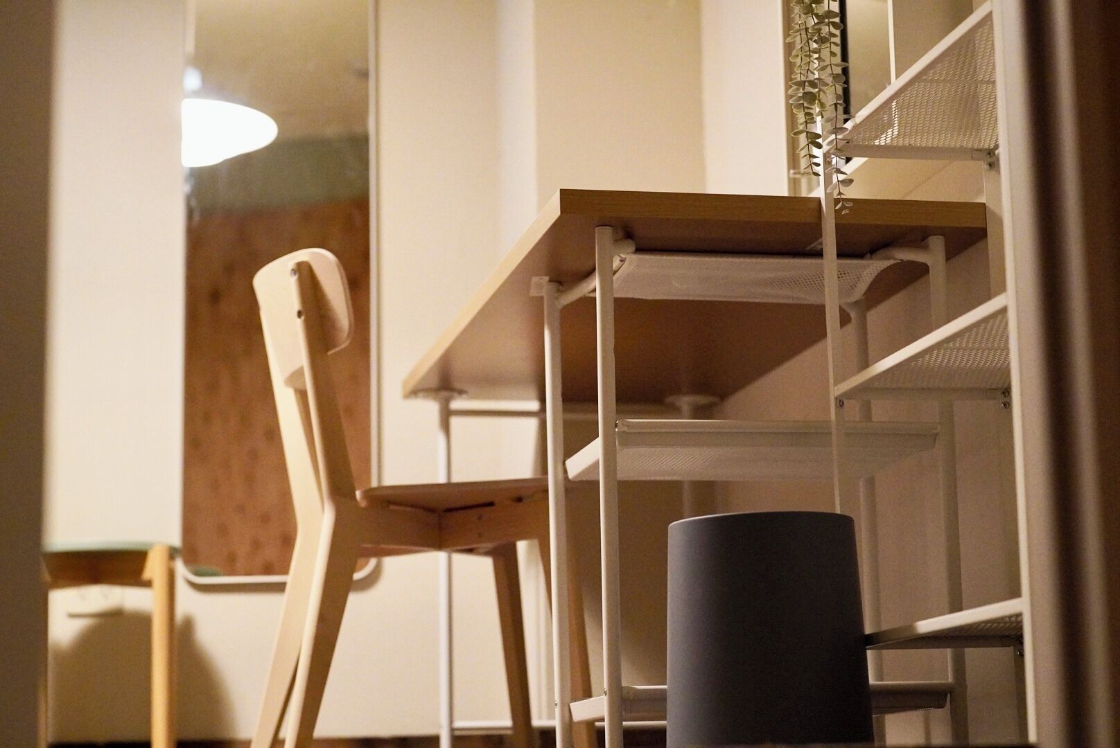 A room with a wooden table and a chair, a white shelf unit, and a cylindrical object on the floor.