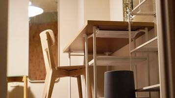 A room with a wooden table and a chair, a white shelf unit, and a cylindrical object on the floor.