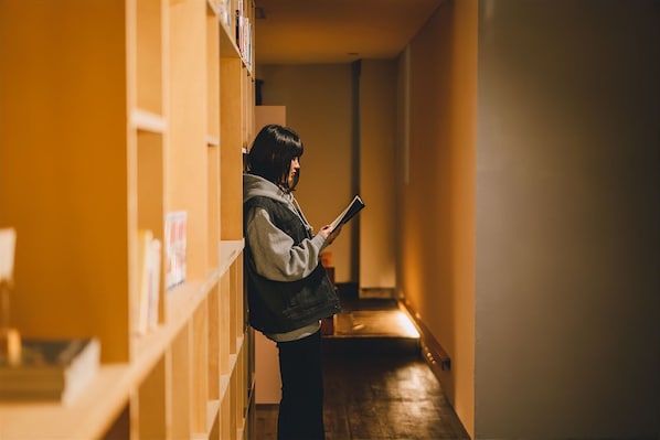 Une personne se tient dans un couloir, avec des étagères à livres d’un côté et un plancher en bois.