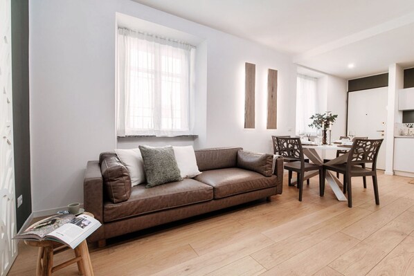 A modern living room with a brown leather sofa, a dining table with chairs, and a kitchen in the background. - Rafael White Home - MyHomeinComo (Como)