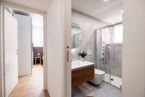 A modern bathroom with a glass shower enclosure, a wooden vanity, and a round mirror. - Rafael White Home - MyHomeinComo (Como)