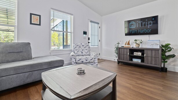 A modern living room with a grey sofa, a patterned armchair, a wooden coffee table, and a TV displaying 'iTrip Palm Harbor'. - Spacious Getaway Near FL Attractions, Plunge Pool, Game Room, Firepit, BBQ, Pet-Friendly & Sleeps 10 (Brooksville)