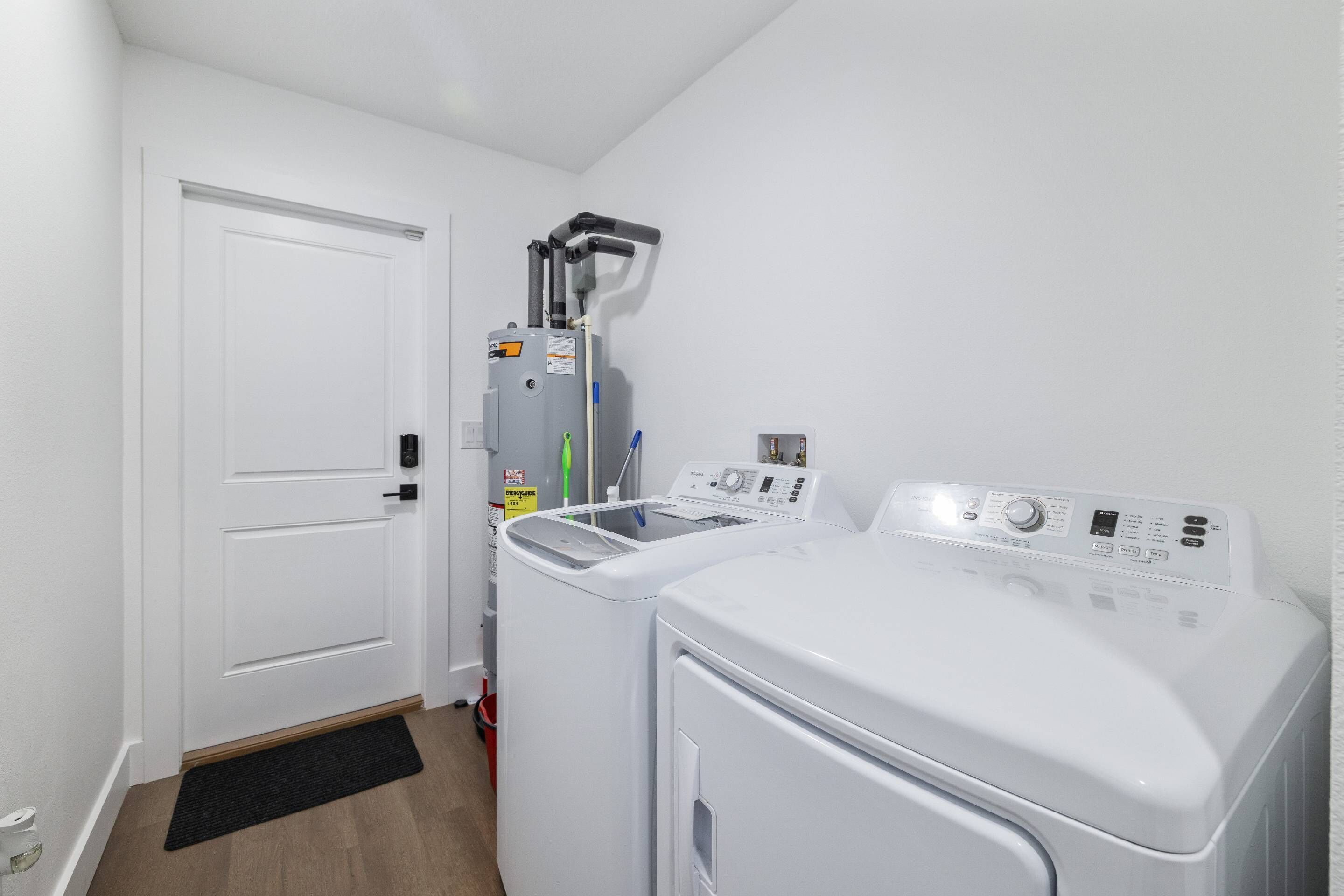 A laundry room with a front-loading washer and dryer, a water heater, and a door.